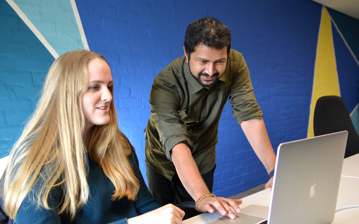 An Electrum Software Developer mentor coaching an intern in front of a Macbook screen